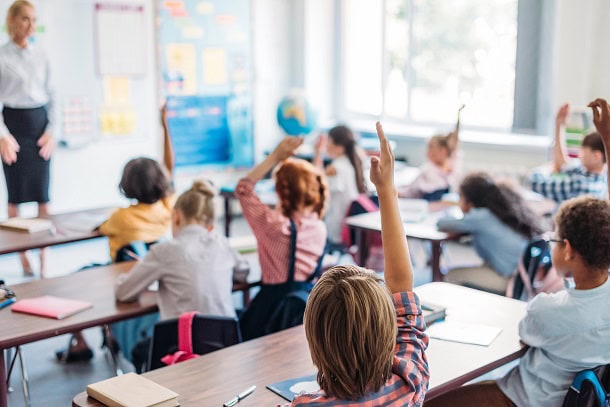 Kids sitting in class with their hand up.