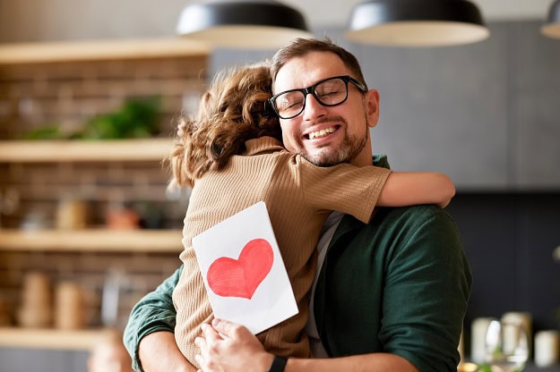 A happy Father hugging his child while holding a Father's Day card.