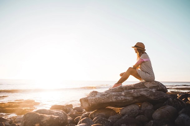 A woman sitting on a rock by the ocean and watching the view.