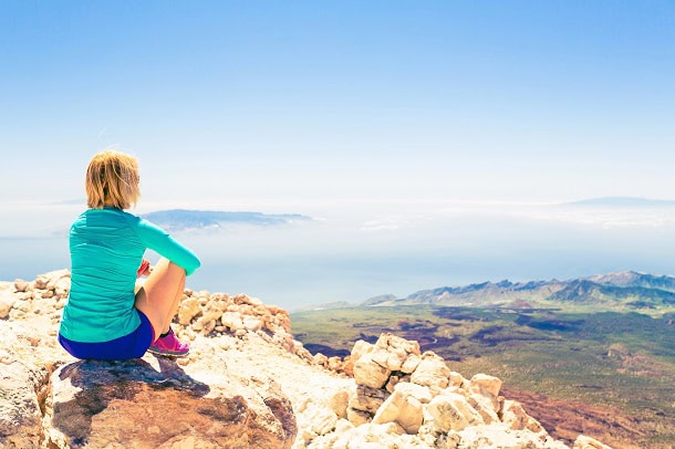A woman on the top of a mountain looking at the vast view before her.