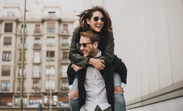 A happy couple outside with the man giving the woman a piggyback ride.