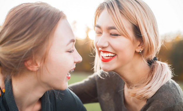 Two women laughing outdoors in the sun.