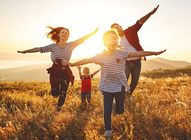 A happy family running towards the camera in a field of grass with their arms stretched out imitating airplanes.