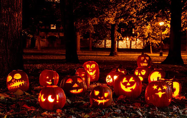A group of carved pumpkins in a park at night with spooky darkness and yellow light.