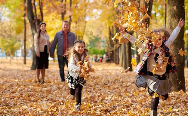 Children running and throwing autumn leaves while their parents watch them smiling.