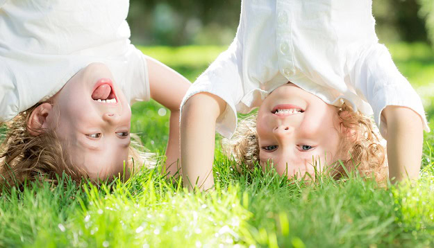 Two kids standing on their hands in the grass and laughing.
