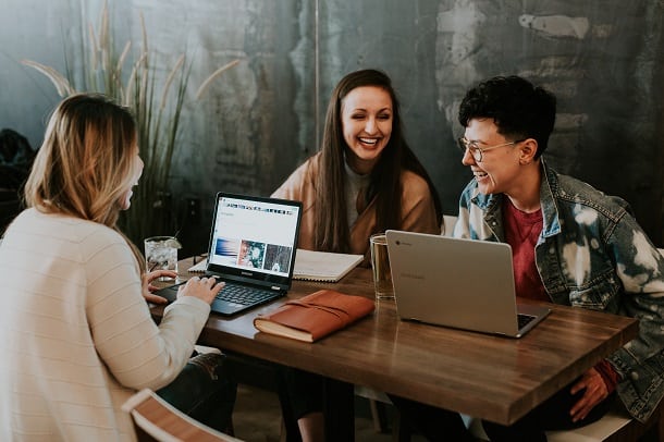 Three women with laptops laughing.