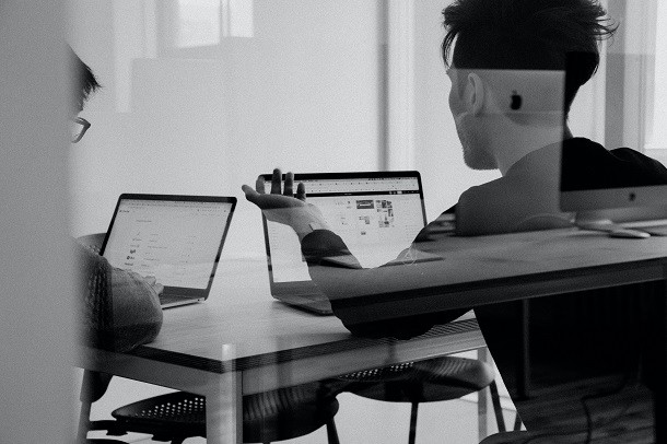 Two people discussing something while looking at their laptops.