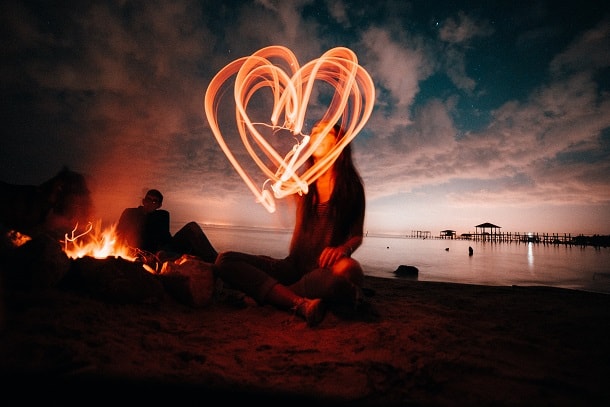 A woman making a heart in the air with a glow stick during an evening at the beach.