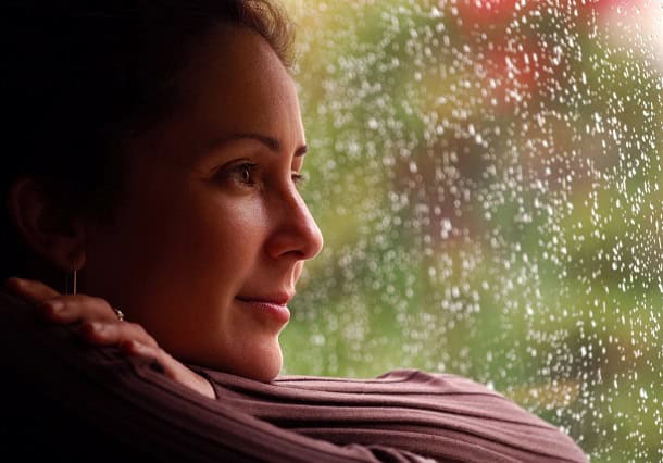 Woman looking out of rainy window with a slight smile on her face.