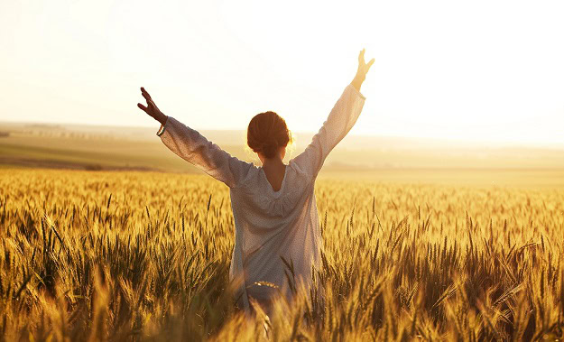 A woman in a field in summer with her arms stretched towards the sky.