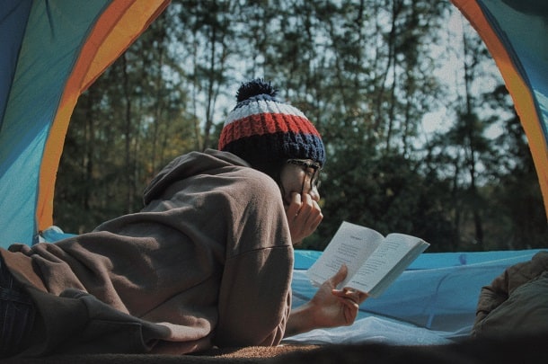 Woman reading a book while camping in the forest.