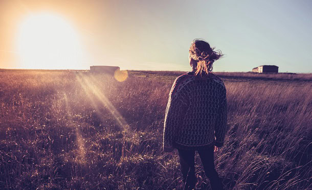 Woman looking at the sunset while standing in a late summer field.