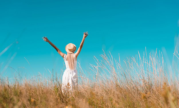 Woman in a field stretching her arms towards the blue sky.