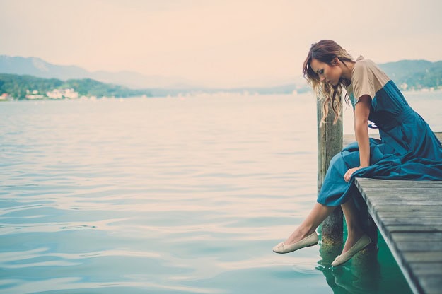 A woman sitting on a pier with mountain lake view.