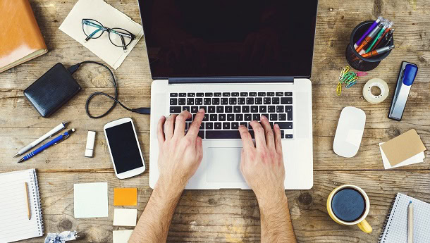 A man working with a laptop with a coffee cup and other things on his desk.