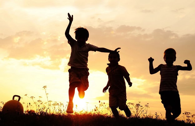 Happy kids running in the grass at sunset.