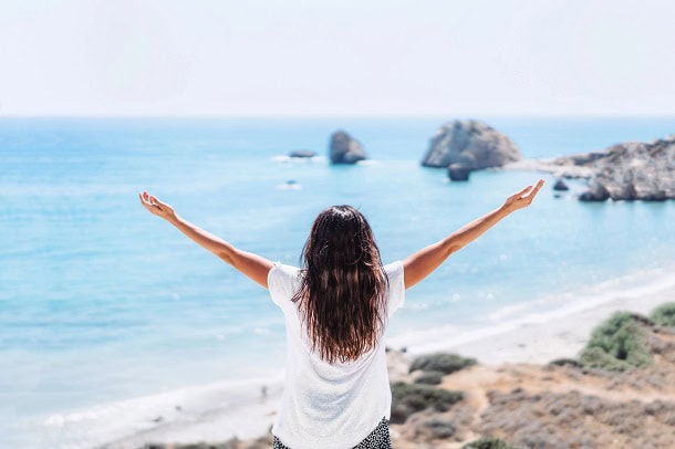 A woman raising her hand while watching the view at the ocean.