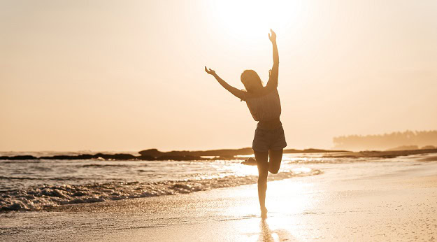 A happy woman dancing on the beach by the waters edge.