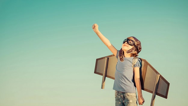 A boy with wings looking up at the sky with his arm raised.