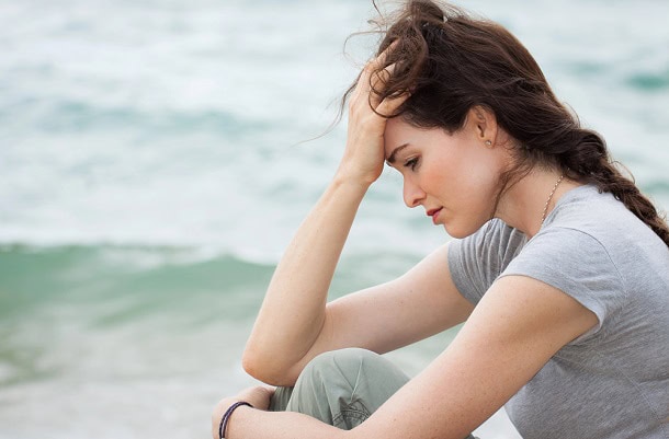A thoughtful and upset woman sitting by the beach.